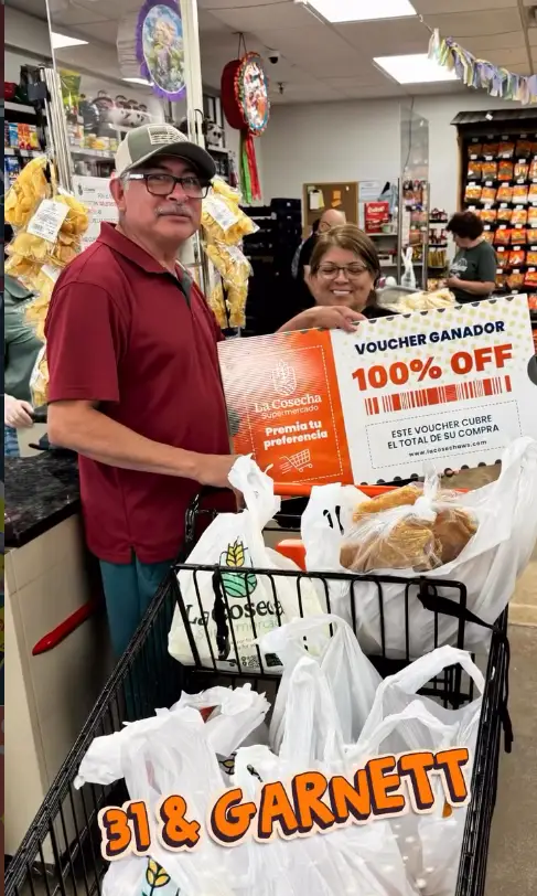 Pareja ganadora en La Cosecha Supermercado Tulsa mostrando su voucher del 100% de descuento en su compra junto a su carrito de mandado.